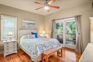 Quarto com cama, mesa de cabeceira, luminária, ventilador de teto e vista para um deck exterior através de uma porta de correr de vidro.