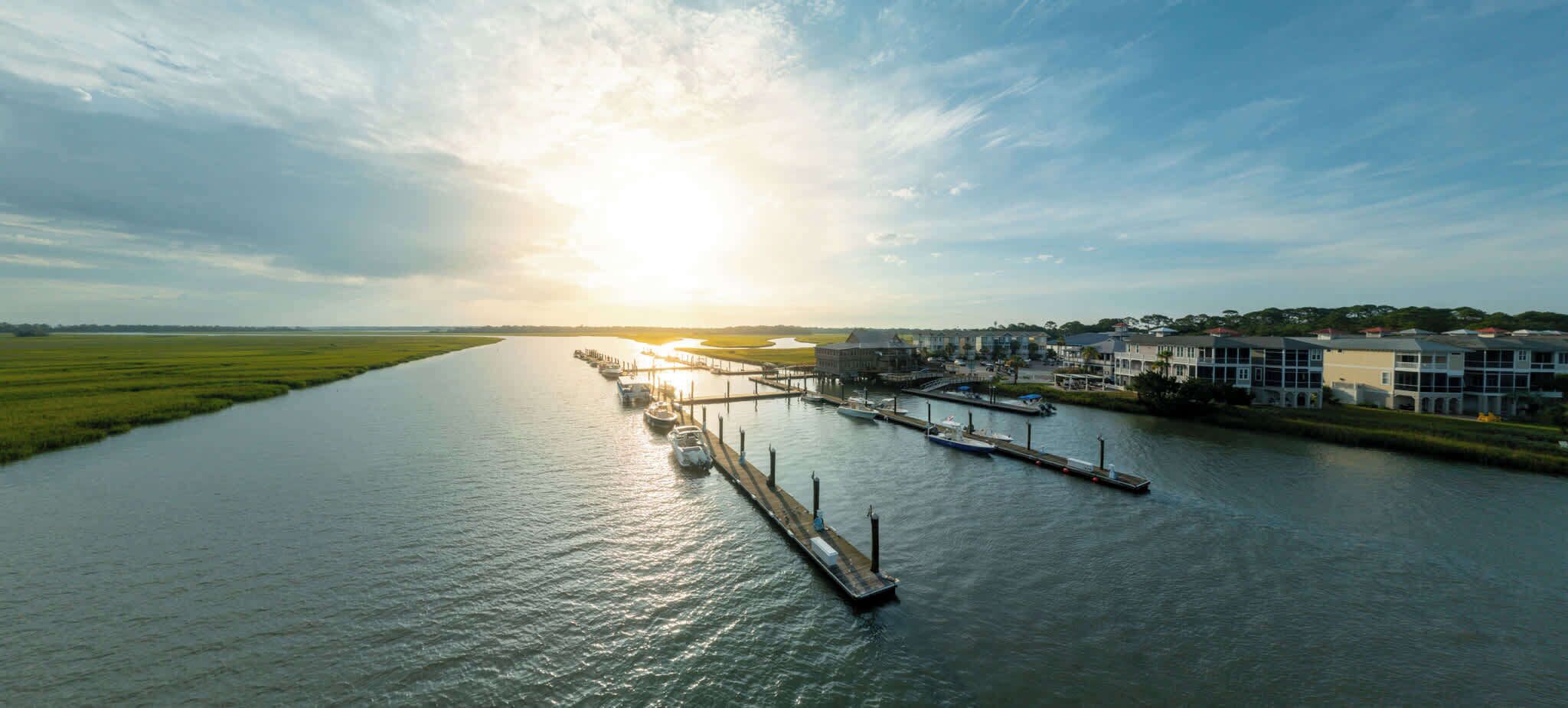 A riverfront marina with boats docked, a pier, and buildings along the riverbank.