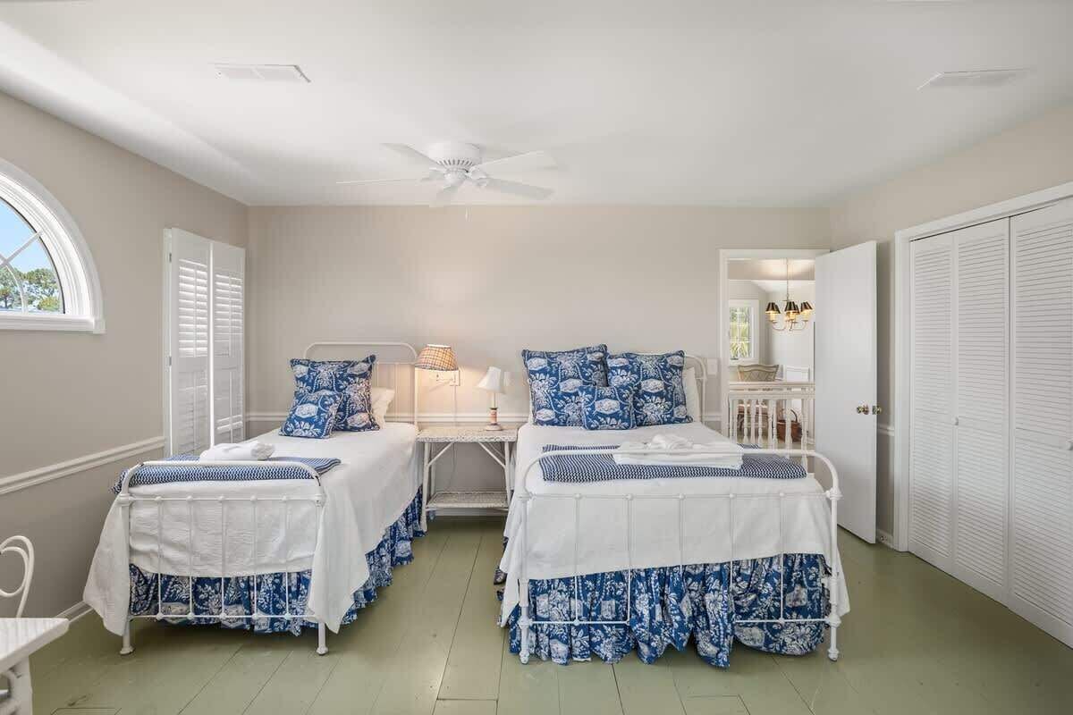 A bedroom with two beds, a ceiling fan, a window, and a door.