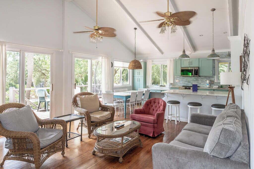 A spacious living area with wicker furniture, a grey sofa, and a kitchen with teal cabinets.