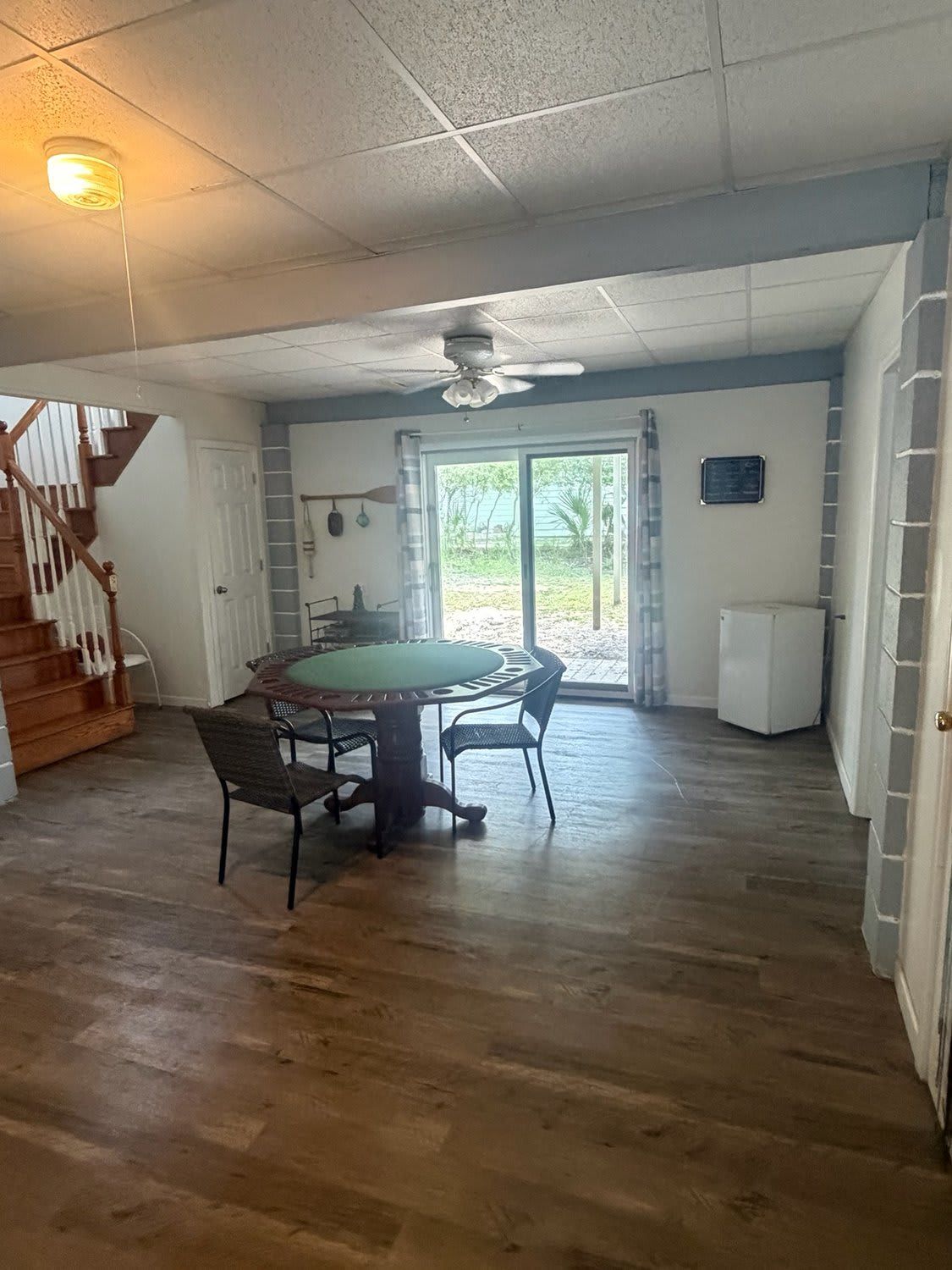A room with a wooden floor, a dining table with chairs, a ceiling fan, a staircase, and a door leading outside.