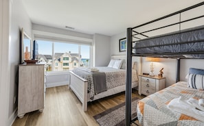 Une chambre avec un lit superposé, une table de chevet, une lampe et une vue sur les maisons par la fenêtre.