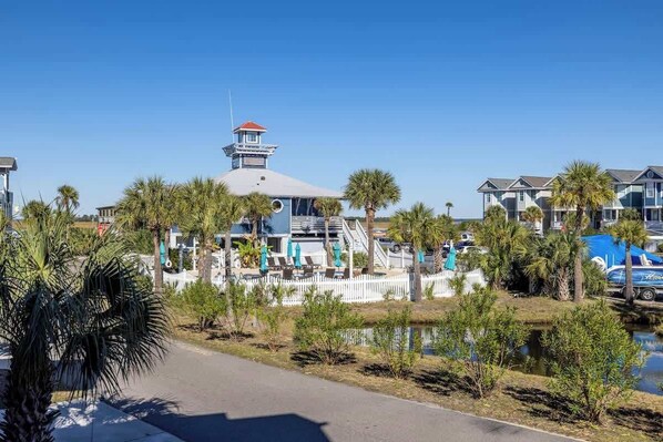 A waterfront hotel with a lighthouse, palm trees, and a white picket fence.