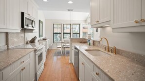 A kitchen with white cabinetry, granite countertops, a central island, and a view through large windows. - 112 Capt John Fripp Villa (Fripp Island)