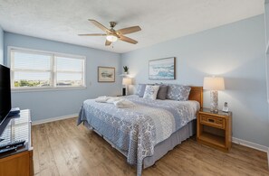 A bedroom with a bed, a ceiling fan, a window, and a nightstand with a lamp. - 143 Captain John Fripp Villa - The Lone Palm (Fripp Island)