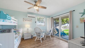 A room with a bed, a desk, a chair, a ceiling fan, and a view through a glass door.