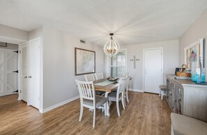 A dining area with a wooden table and white chairs, a chandelier, and a map on the wall. - 143 Captain John Fripp Villa - The Lone Palm (Fripp Island)