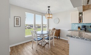 A kitchen with a dining area, wooden flooring, a hanging light fixture, and a view of the outdoors. - 143 Captain John Fripp Villa - The Lone Palm (Fripp Island)