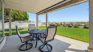 A covered patio with a table and chairs, overlooking a well-maintained lawn and a distant view.