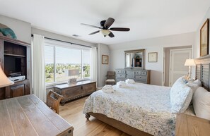 Ein Schlafzimmer mit Bett, Schreibtisch, Stuhl, Kommode, Deckenventilator und einem Fenster mit Jalousien.