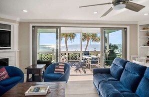 Een woonkamer met een bank, fauteuil en salontafel, een televisie, en een balkon met uitzicht op de oceaan.