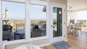 Une pièce dotée d’une porte-fenêtre coulissante donnant sur un patio extérieur aménagé avec des meubles en osier et offrant une vue sur le paysage.