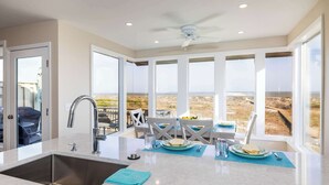 Une cuisine équipée d’un évier, un coin repas avec une table et des chaises, et de grandes fenêtres offrant une vue sur le paysage.