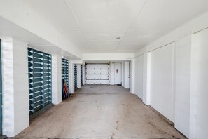 Un long couloir étroit aux murs blancs et au sol en béton, qui mène à une porte fermée au bout.