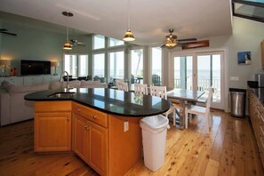 A modern kitchen with a central island, wooden cabinets, and a dining area with a table and chairs. - 407 Ocean Point Lane (Fripp Island)
