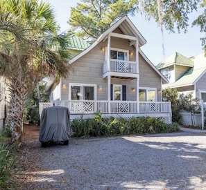 A two-story house with a balcony, a covered grill, and a gravel driveway.