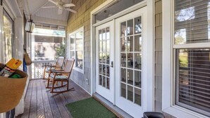 Eine überdachte Veranda mit Holzboden, weißen Glastüren und einem Deckenventilator.