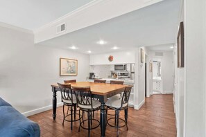 Un comedor con una mesa y sillas de madera, una cocina al fondo y un pasillo que conduce a otras habitaciones.
