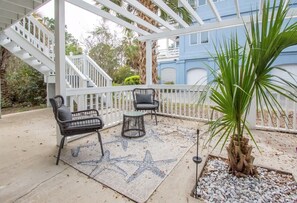 A covered patio area with a star-patterned rug, two black chairs, a small round table, and a palm plant.