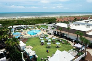 A rooftop pool area with a view of the beach, surrounded by palm trees and outdoor seating.