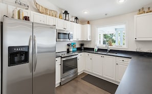 A modern kitchen with white cabinets, stainless steel appliances, and a window providing natural light. - 758 Marlin Drive (Fripp Island)