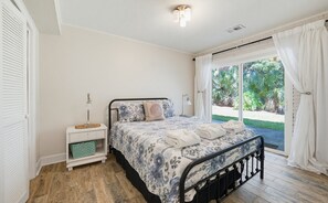 A bedroom with a bed, bedside tables, a radiator, and a view of greenery outside.
