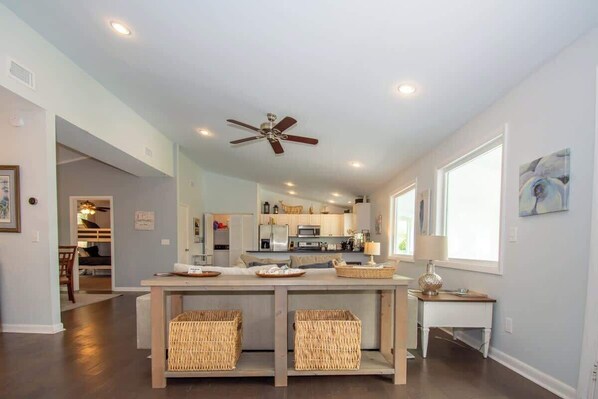 A modern kitchen with a central island, overhead ceiling fan, and large windows.