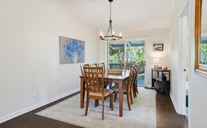 A dining area with a chandelier, wooden chairs, a table, a rug, and artwork on the wall.