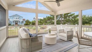 A covered porch with white wicker furniture, a ceiling fan, and a view of a blue house. - 721 Sea Dragon Lane (Fripp Island)