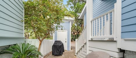 A narrow paved pathway leading to a covered barbecue area, flanked by a white fence and a palm tree.
