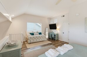 Un dormitorio con cama, escritorio, silla, televisor y puerta.