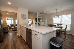 Cozinha moderna com ilha central, eletrodomésticos de aço inoxidável e área de jantar com cadeiras de madeira.