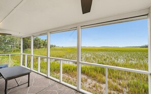 A covered outdoor area with a table and chairs, large windows offering a view of a rice field.