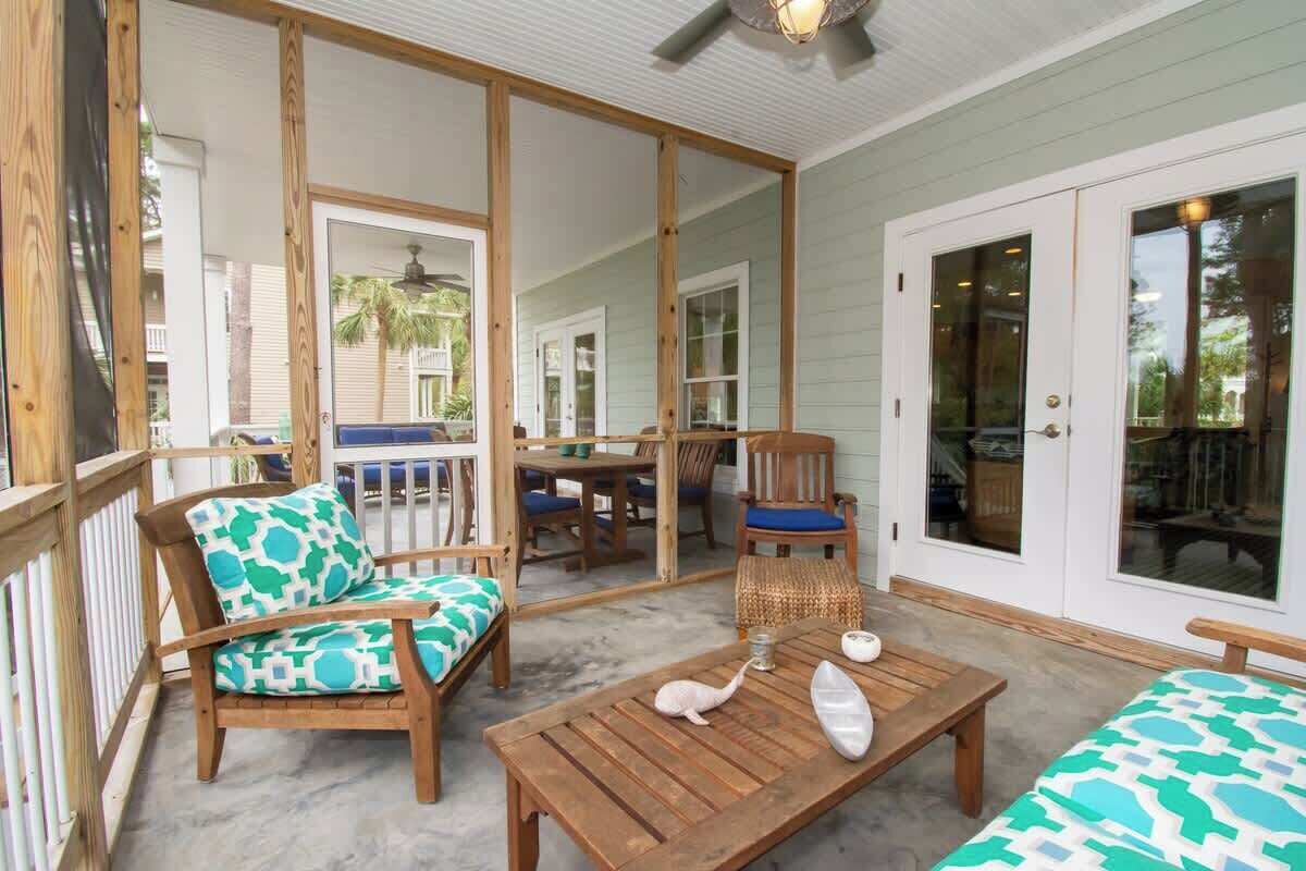 A covered outdoor patio with wooden furniture, including chairs and a table, and a sliding glass door leading to an interior space.