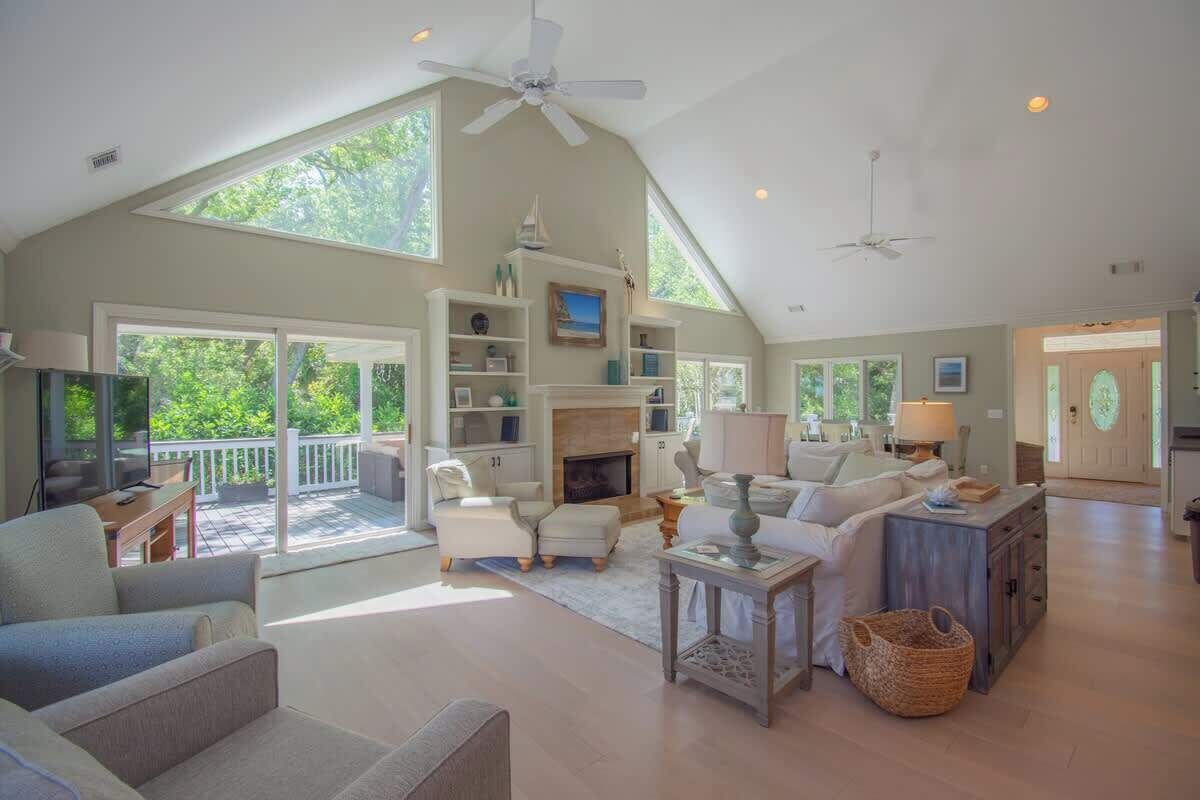 A spacious living room with a high ceiling, large windows, and a fireplace.