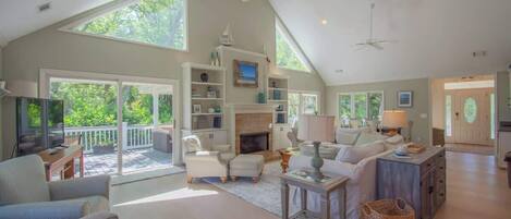 A spacious living room with a high ceiling, large windows, and a fireplace.