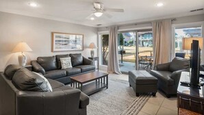 A modern living room with a sofa, coffee table, and TV, large windows with curtains, and a ceiling fan. - 327 Capt John Fripp Villa (Fripp Island)