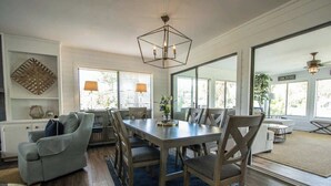 A dining area with a table and chairs, a sofa, and a large window with blinds. - 377 Tarpon Blvd (Fripp Island)