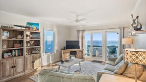 A living room with a TV, bookshelves, a sofa, and a view of the ocean. - 625 Newhaven (Fripp Island)