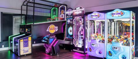 Una hilera de máquinas de videojuegos arcade, incluyendo baloncesto y juegos de garra, con un aro de baloncesto y una exhibición de recuerdos de los Lakers de la NBA.