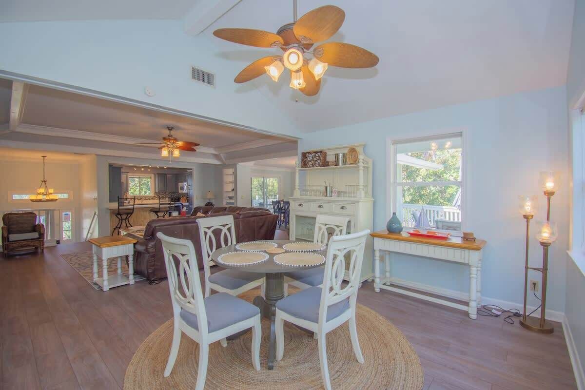 Un vaste espace de vie comprenant une table à manger, des chaises blanches, un ventilateur de plafond et une vue sur l’extérieur.
