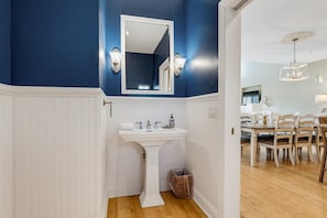 A bathroom with a white pedestal sink, a mirror above it, and a trash can. - 125 Ocean Creek Blvd (Fripp Island)
