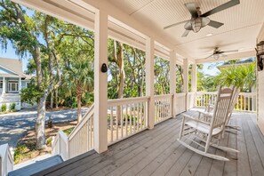 A covered porch with a ceiling fan, white railings, and a view of a residential street with trees.
