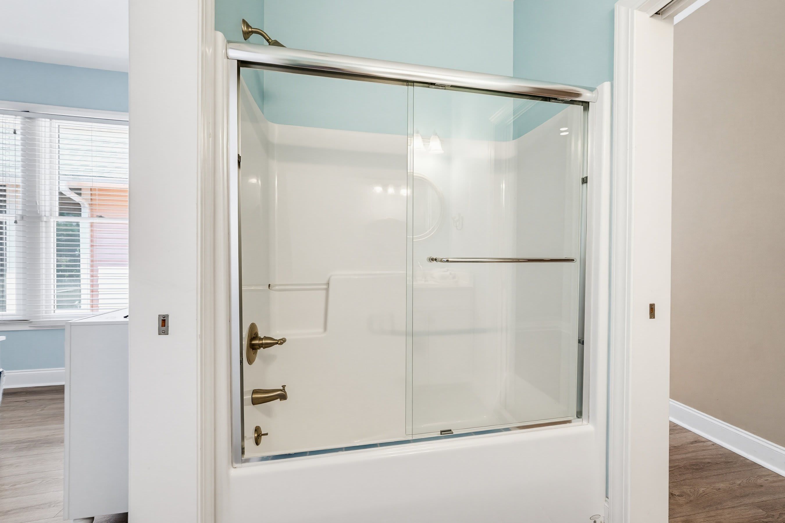 A glass-enclosed shower stall with a white exterior and brass fixtures.