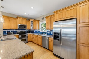 A modern kitchen with wooden cabinets, stainless steel appliances, and blue tile backsplash.