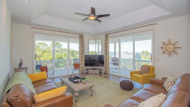 A spacious living room with a television, leather sofas, a coffee table, and a balcony with a view. - 619 Porpoise Circle (Fripp Island)