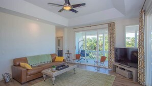 A spacious living room with a ceiling fan, a large window, a sofa, a coffee table, and a TV. - 619 Porpoise Circle (Fripp Island)