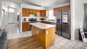 Una cocina moderna con armarios de madera, una isla central, electrodomésticos de acero inoxidable y suelo de baldosas.
