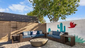 Un patio al aire libre con un conjunto de sofá de mimbre, un brasero y un mural de cactus en la pared.