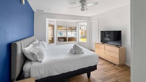Un dormitorio con cama, televisor, ventilador de techo y vistas a un espacio exterior.